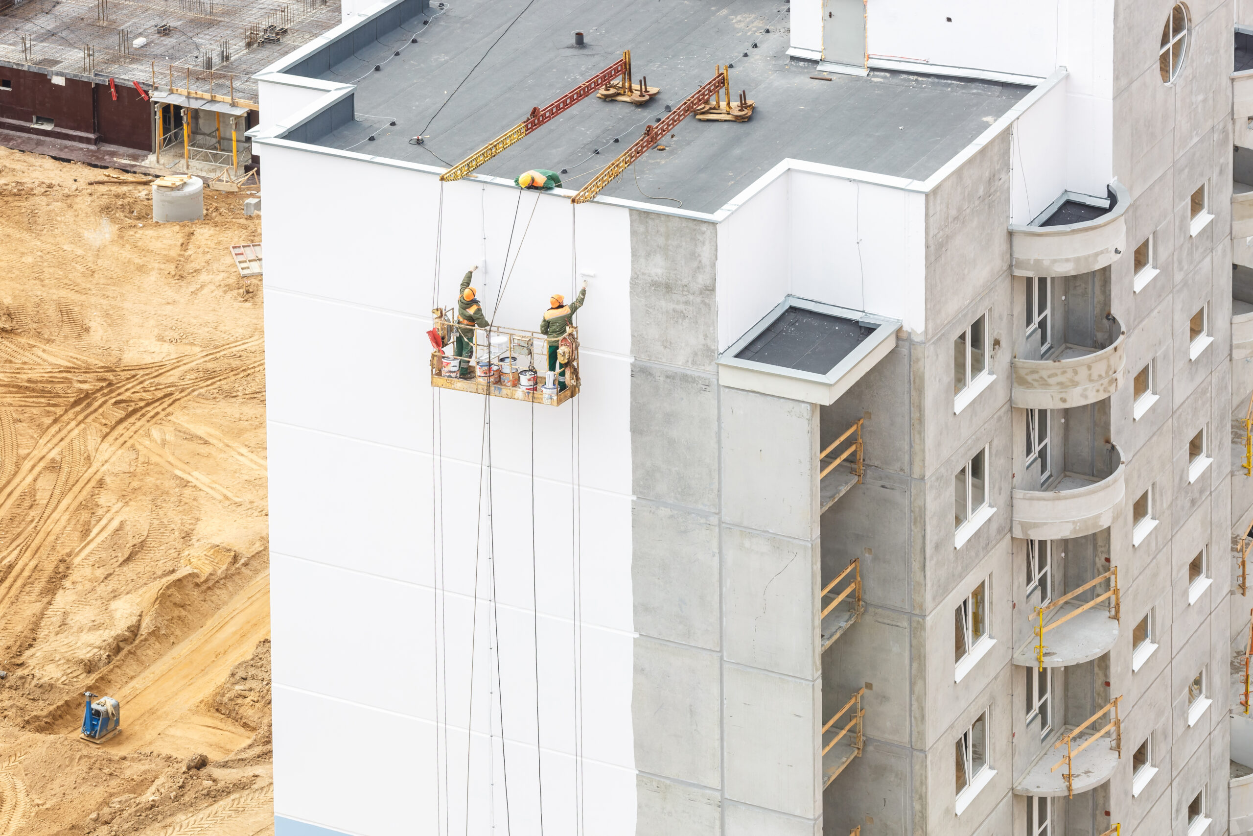 workers in a crane paint the wall of a residential high-rise bui